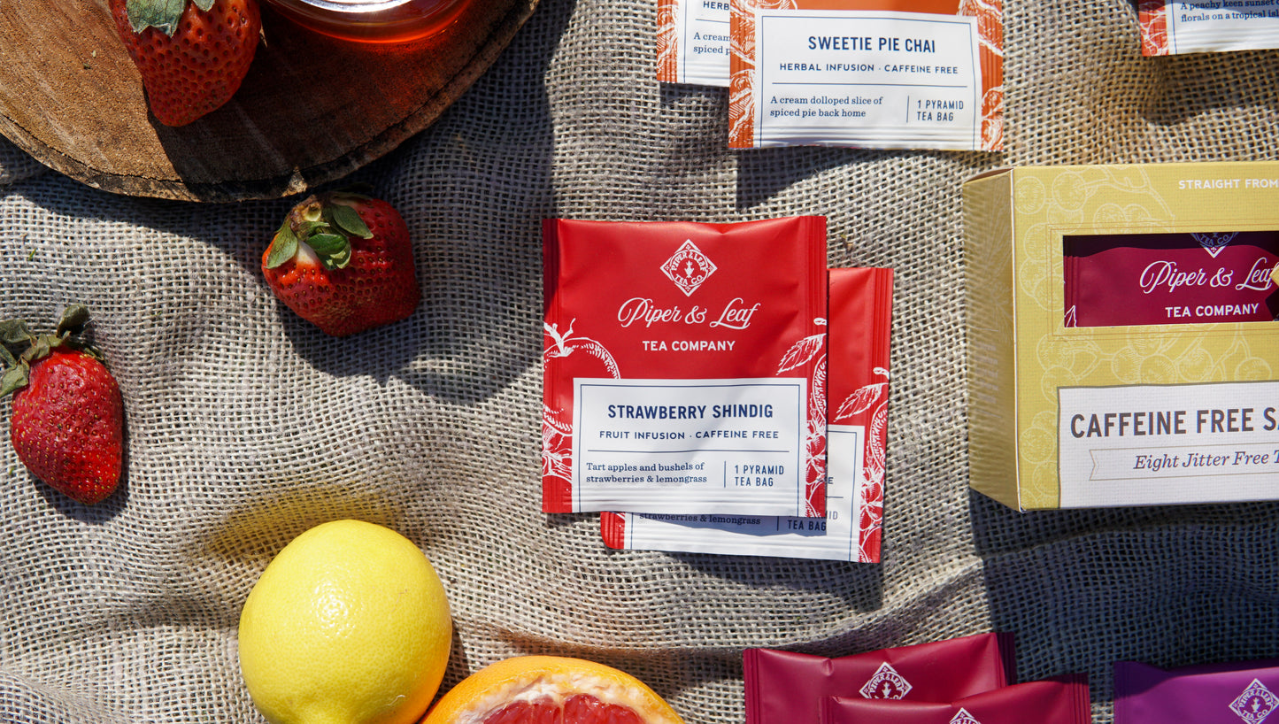 Piper & Leaf Tea Co.’s Caffeine Free Sampler (box of 16 tea bags) is displayed on burlap, surrounded by a lemon, grapefruit, and other tea boxes.