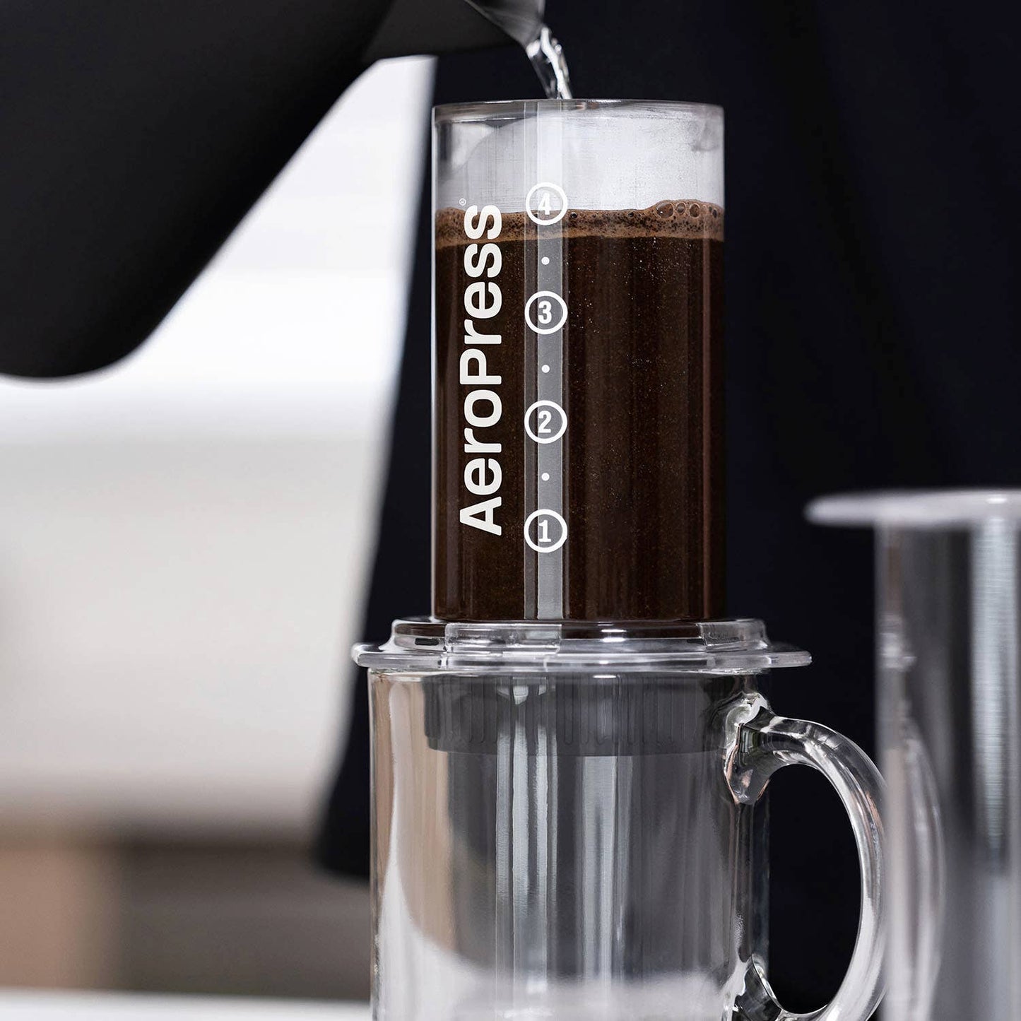 A person pours hot water into an AeroPress coffee maker equipped with AeroPress Paper Micro-Filters, carefully placed over a glass mug.