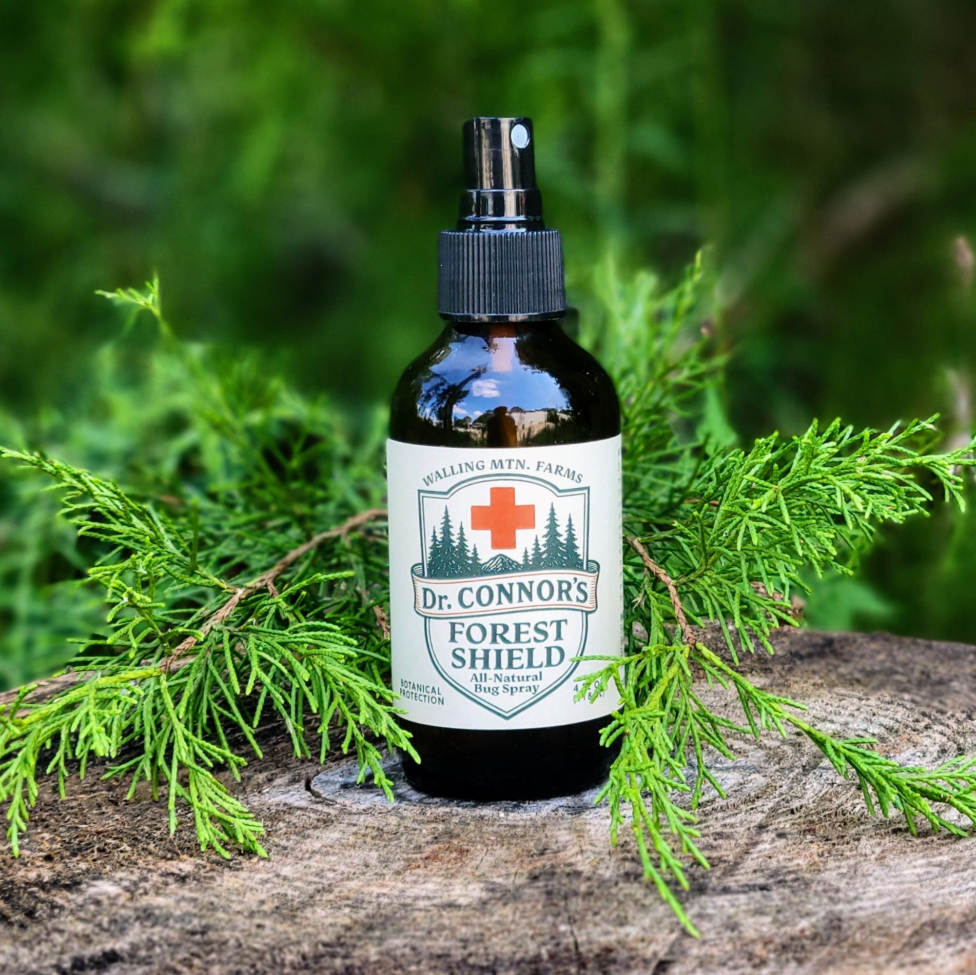 A bottle of Walling Mountain Farms' Dr. Connor's Forest Shield All-Natural Bug Spray, a DEET-free insect repellent, sits on a tree stump with green foliage in the background.