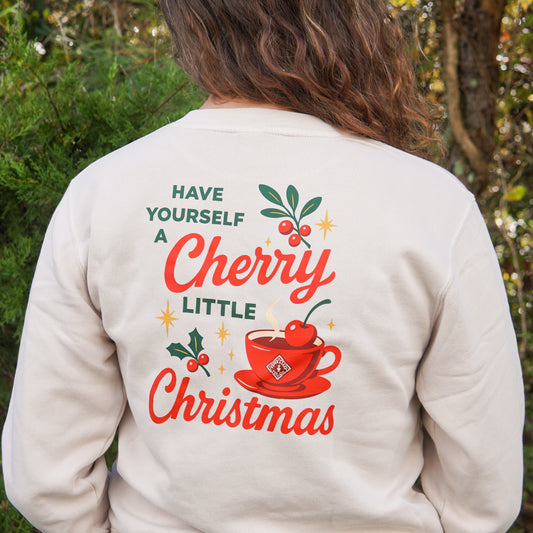 Celebrate the season in Piper & Leaf Tea Co.'s "A Cherry Little Christmas Shirt," a cream-colored sweatshirt featuring a festive red teacup and holly—perfect gift for tea lovers.