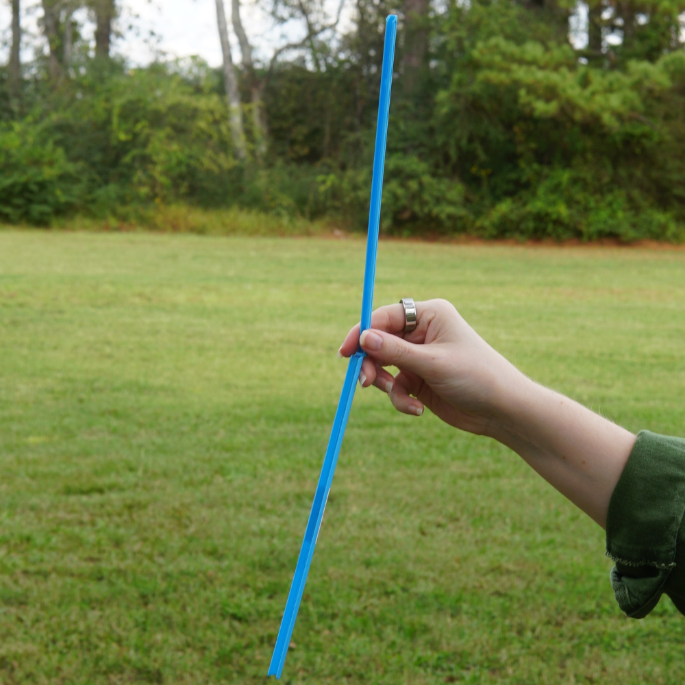 A person holds an UnStraw from Piper & Leaf Tea Co., outdoors with a grassy field and trees in the background.