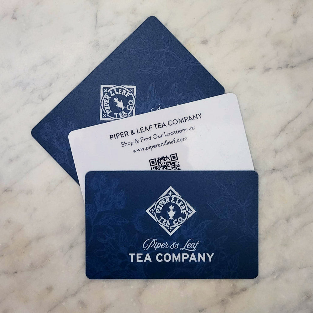A trio of blue gift cards with berries, flowers, & herbs beneath the Piper & Leaf logo. Front: "Piper & Leaf Tea Company" Back: "Shop & Find Our Locations at: www.piperandleaf.mom"
